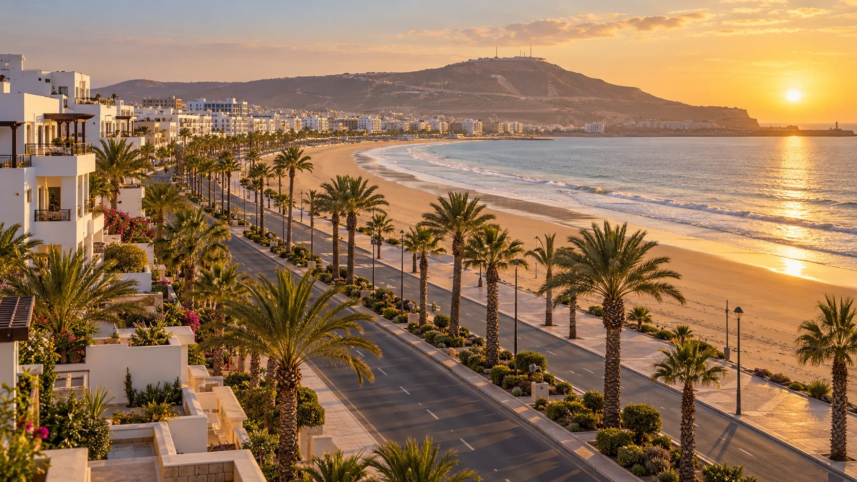 Golden-hour view of whitewashed low-rise apartment blocks along Agadir's palm-lined beach promenade facing the Atlantic Ocean
